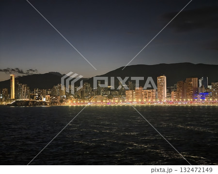 tranquil seaside panorama during twilight featuring illuminated waterfront and distant mountains 132472149