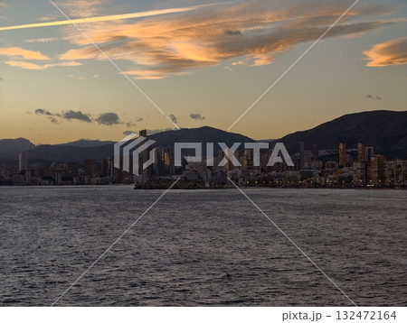 soothing shoreline scenery with calm harbor filled with boats and distant mountain silhouettes soothing shoreline scenery with calm harbor filled with boats and distant mountain silhouettes 132472164