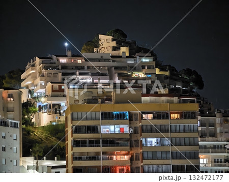 nighttime view of illuminated apartment terraces overlooking bustling waterfront skyline on coastal 132472177