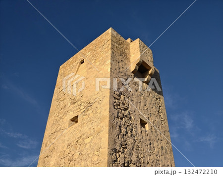 sunlit ancient stone structure, solitary stone watchtower crafted from rough masonry against clear sunlit ancient stone structure, solitary stone watchtower crafted from rough masonry against clear 132472210