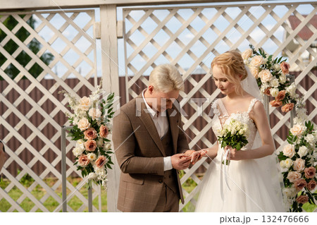 Couple exchanges wedding rings during outdoor ceremony surrounded by flowers Couple exchanges wedding rings during outdoor ceremony surrounded by flowers 132476666