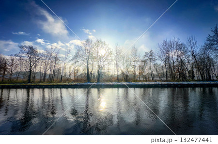 A Serene and Tranquil Winter Reflection at the Riverbank with Beautiful Glowing Sunlight 132477441