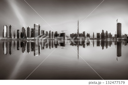 Monochrome city skyline with tall skyscrapers reflecting on calm water under a cloudy sky, Dubai Marina bay UAE Monochrome city skyline with tall skyscrapers reflecting on calm water under a cloudy sky, Dubai Marina bay UAE 132477579