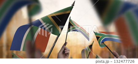 South Africa flags in their hands on a blurred urban background South Africa flags in their hands on a blurred urban background 132477726