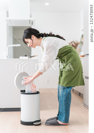 キッチンでゴミ箱のゴミをまとめるエプロン姿の女性,主婦 132478093