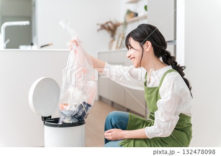 キッチンでゴミ箱のゴミをまとめるエプロン姿の女性,主婦 132478098