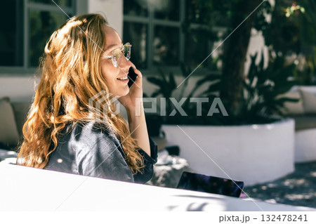 Young Woman with Red Hair Talking on Phone Outdoors in a Modern Garden Workspace Young Woman with Red Hair Talking on Phone Outdoors in a Modern Garden Workspace 132478241