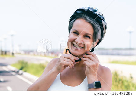 Smiling active woman fastening bike helmet before outdoor ride on a bright sunny day in summer Smiling active woman fastening bike helmet before outdoor ride on a bright sunny day in summer 132478295