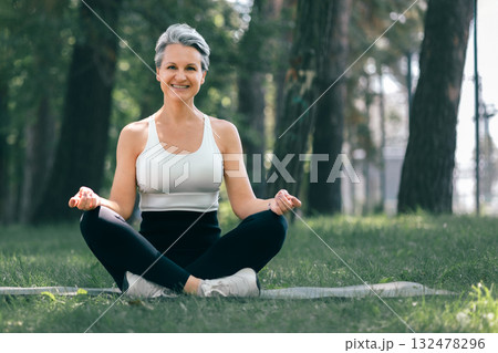 Smiling Mature Woman Practicing Yoga and Meditation in the Park on a Sunny Summer Day Smiling Mature Woman Practicing Yoga and Meditation in the Park on a Sunny Summer Day 132478296