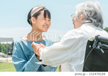 車椅子に乗るおばあちゃんに花束をプレゼントする笑顔の孫娘 132479189