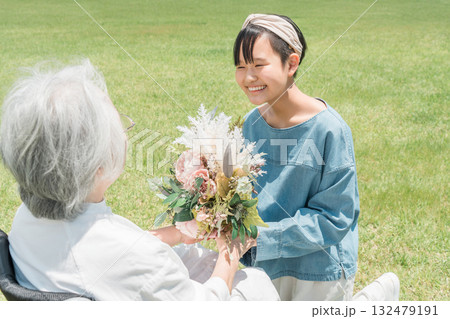 車椅子に乗るおばあちゃんに花束をプレゼントする笑顔の孫娘 132479191
