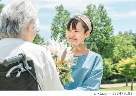車椅子に乗るおばあちゃんに花束をプレゼントする笑顔の孫娘 車椅子に乗るおばあちゃんに花束をプレゼントする笑顔の孫娘 132479192