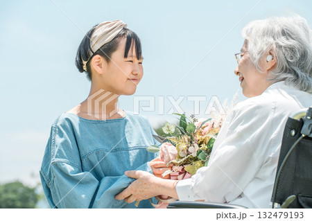 車椅子に乗るおばあちゃんに花束をプレゼントする笑顔の孫娘 132479193