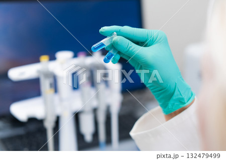 Female scientist in lab coat studying blue liquid in test tube used for DNA analysis and biochemical research. Female scientist in lab coat studying blue liquid in test tube used for DNA analysis and biochemical research. 132479499