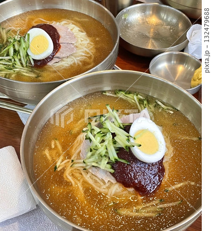Cold and refreshing Korean naengmyeon noodles, served in a chilled broth with sliced cucumber, radish, and a boiled egg. A savory, tangy dish ideal for hot summer days. 132479688