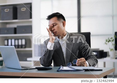 Sad businessman is sitting at table, covering his face with his hand. On desk is laptop, tablet computer, Stress. Sad businessman is sitting at table, covering his face with his hand. On desk is laptop, tablet computer, Stress. 132482994