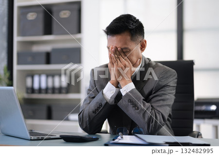Sad businessman is sitting at table, covering his face with his hand. On desk is laptop, tablet computer, Stress. Sad businessman is sitting at table, covering his face with his hand. On desk is laptop, tablet computer, Stress. 132482995