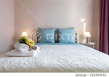 Cozy Bedroom Interior with Blue Pillows and Fresh Towels on Bed Cozy Bedroom Interior with Blue Pillows and Fresh Towels on Bed 132484202