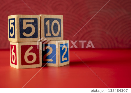Stack of wooden number blocks with various numbers on a red background 132484307