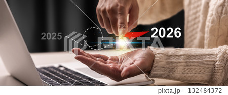Female hand with laptop showing a flying plane from 2025 to 2026 on a virtual screen. Happy New Year concept or Celebration 132484372