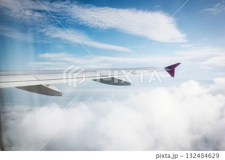 The image shows an airplane wing viewed from a passenger window seat. The sky is partially cloudy with blue sky visible, and sunlight is illuminating the scene, suggesting it could be daytime. The The image shows an airplane wing viewed from a passenger window seat. The sky is partially cloudy with blue sky visible, and sunlight is illuminating the scene, suggesting it could be daytime. The 132484629