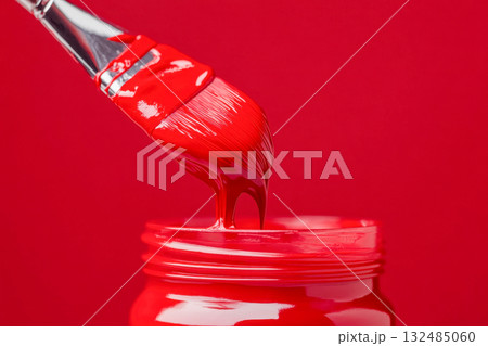 Vivid red paint drips from a brush into a jar, set against a bright red backdrop, capturing a moment of artistic expression Vivid red paint drips from a brush into a jar, set against a bright red backdrop, capturing a moment of artistic expression 132485060