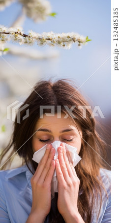 Woman sneezing into tissue during spring allergy season Woman sneezing into tissue during spring allergy season 132485185