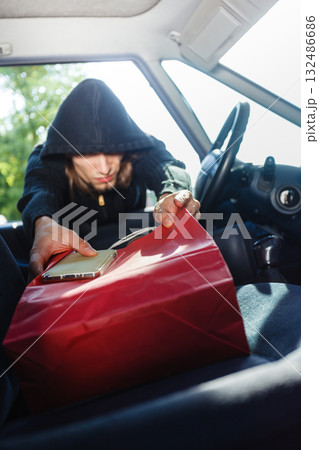 Burglar thief stealing smartphone and bag from car Burglar thief stealing smartphone and bag from car 132486686