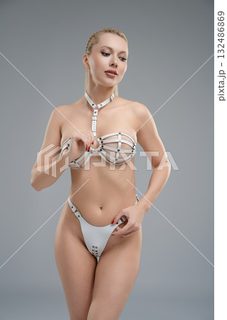 Woman in leather belts poses confidently in a studio setting with a simple gray backdrop 132486869