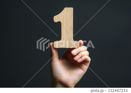 Hand holding a wooden number one sign against a dark background for celebration or marking an event Generative AI Hand holding a wooden number one sign against a dark background for celebration or marking an event Generative AI 132487233