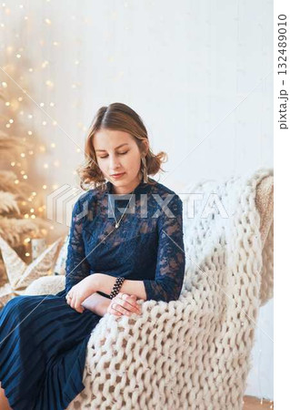 teenage girl in a dress near an unconventional Christmas tree surrounded by golden lights 132489010
