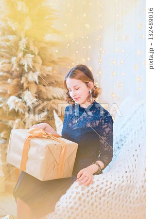 teenage girl in a dress near an unconventional Christmas tree surrounded by golden lights teenage girl in a dress near an unconventional Christmas tree surrounded by golden lights 132489016