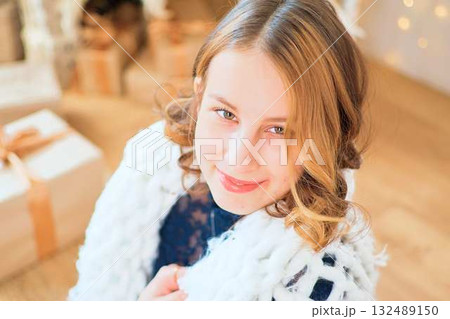teenage girl in a dress near an unconventional Christmas tree surrounded by golden lights 132489150
