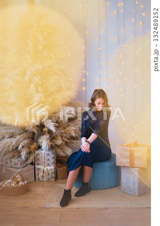 teenage girl in a dress near an unconventional Christmas tree surrounded by golden lights teenage girl in a dress near an unconventional Christmas tree surrounded by golden lights 132489152