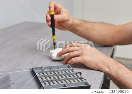 male hands with screwdriver is fixing kids toy on grey table. repair shop, focus on screwdriver set 132490036