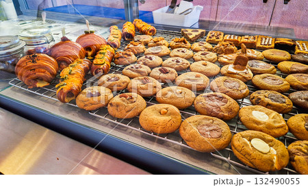 A variety of cookies displayed in a bakery. The assortment includes chocolate chip, oatmeal, and peanut butter cookies on a cooling rack. 132490055