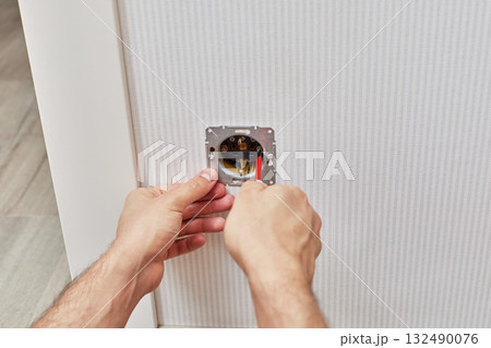 male hands installing electrical wall outlets with a screwdriver at home 132490076