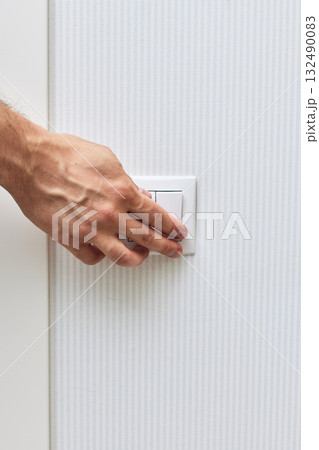 male finger is turning on or off on white light switch on blue wall. 132490083