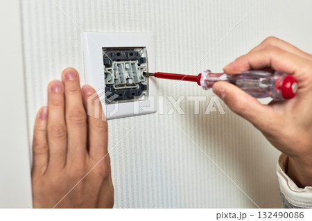 electrician installing electric light switch using screwdriver at home, close-up electrician installing electric light switch using screwdriver at home, close-up 132490086
