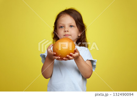 cute Caucasian little child girl holding grapefruit on yellow background cute Caucasian little child girl holding grapefruit on yellow background 132490094
