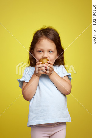 cute Caucasian little child girl holding kiwi fruit on yellow background 132490110