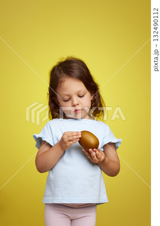 cute Caucasian little child girl holding kiwi fruit on yellow background 132490112