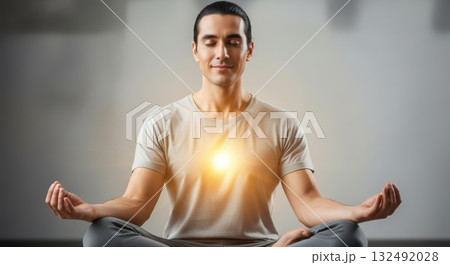 Young man practicing meditation in a serene environment, sitting cross-legged with a glowing light at his heart, embodying peace and mindfulness in a tranquil setting Young man practicing meditation in a serene environment, sitting cross-legged with a glowing light at his heart, embodying peace and mindfulness in a tranquil setting 132492028