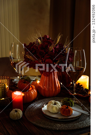 Thanksgiving table setting with decorative pumpkins, candles and string lights on dark wooden table 132492066