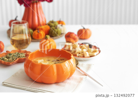 Creamy pumpkin soup with croutons and seeds, served in a pumpkin-shaped bowl on white wooden table. Creamy pumpkin soup with croutons and seeds, served in a pumpkin-shaped bowl on white wooden table. 132492077