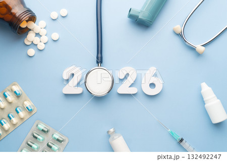 2026 Happy New Year banner for health care and medical concept. Stethoscope with doctor pills, syringe, vaccine vial, eyes drop, antibiotics and white number 2026 on table blue background. 132492247
