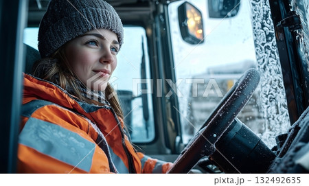 Female driver in warm jacket operates snowplow truck during winter storm in snowy urban area 132492635