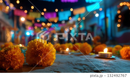 Colorful marigolds and candles adorn an altar for Dia de Muertos. The vibrant street is illuminated with festive lights and papel picado decorations. 132492767