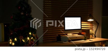 Home office with computer and Christmas tree glowing softly in warm night light 132494720