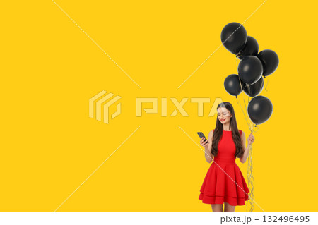 Woman in red dress holds black balloons and uses smartphone 132496495